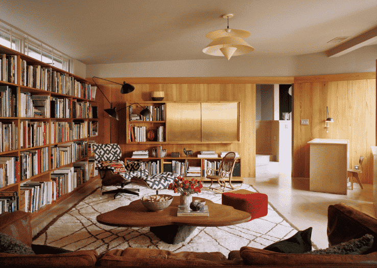 Living room in mid-century modern design with wall of book cases, armchair with coffee table