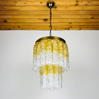 Chandelier with yellow and clear glass design hanging from a wooden ceiling.