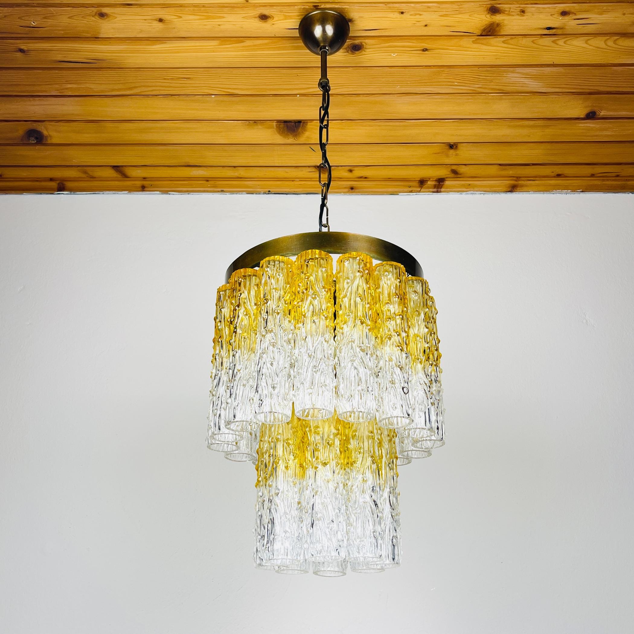 Chandelier with yellow and clear glass design hanging from a wooden ceiling.