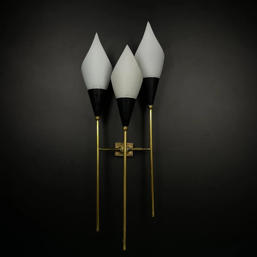 A three-light vintage wall sconce by Stilnovo with white teardrop-shaped glass shades, black conical sections, and gold-toned metal arms, mounted against a dark wall.